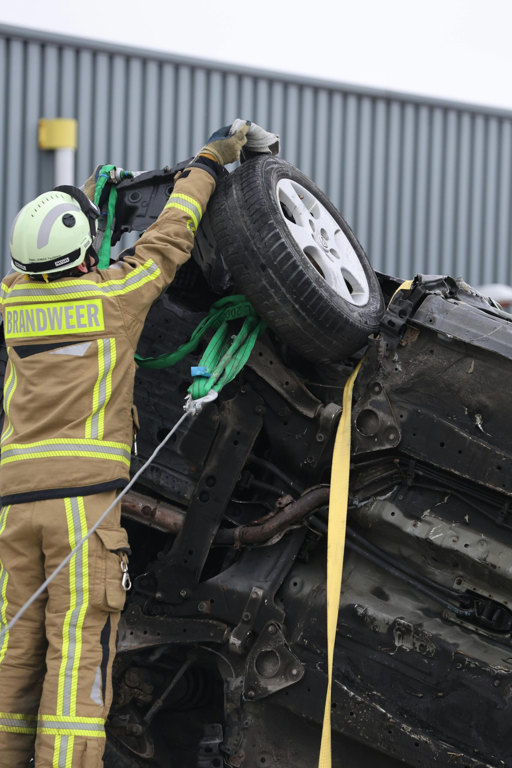 Firefighter in protective gear secures overturned car at an accident scene with ropes and equipment.